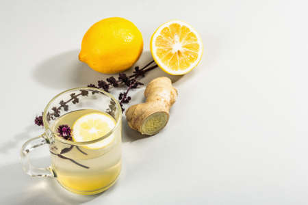 Hot ginger tea with lemon and honey in a glass cup on light gray background. Alternative medicine, natural home remedy for cold and flu, modern hard light, dark shadow, copy spaceの写真素材