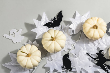 Halloween concept. Ghostly white maple leaves on a branch and white pumpkins. Traditional holiday decor on gray background. A trendy hard light, dark shadow, top viewの写真素材