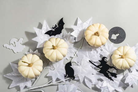 Halloween concept. Ghostly white maple leaves on a branch and white pumpkins. Traditional holiday decor on gray background. A trendy hard light, dark shadow, top viewの写真素材