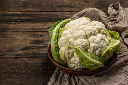 Beautiful cauliflower with green leaves in a ceramic bowl. Vintage napkin, old wooden table, copy spaceの写真素材