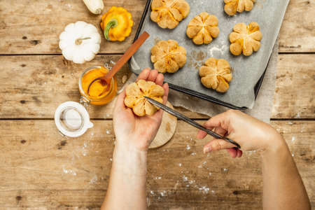 Pumpkin buns or biscuits, traditional fall baked goods. Female hands hold cookies. Seasonal homemade food and autumn decor. Old wooden boards background, top viewの写真素材