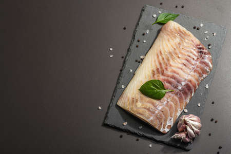 Raw pollock (Pollachius virens) fillet. Fresh fish for healthy food lifestyle. Garlic, sea salt, peppercorn, greens. Black stone concrete background, top viewの写真素材