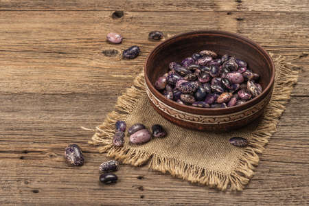Assorted multicolored beans in a ceramic bowl. Raw healthy ingredient for cooking useful food. Old wooden table, copy spaceの写真素材