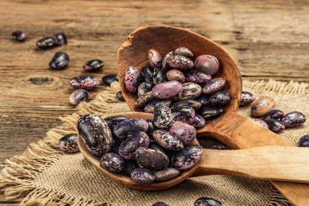Assorted multicolored beans in big wooden spoons. Raw healthy ingredient for cooking useful food. Old wooden table, close upの写真素材