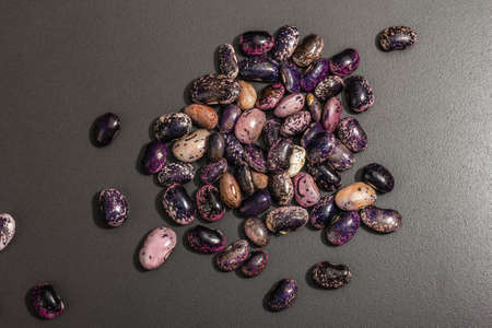 Assorted multicolored beans scattered on black stone background. Raw healthy ingredient for cooking useful food, top viewの写真素材