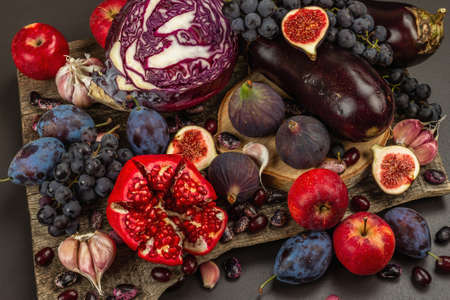 Blue, red and purple food. Culinary background of fruits and vegetables. Fresh figs, plums, onions, eggplant, grapes, cabbage, apples, garlic, dogwood, pomegranate. Black stone background, flat layの写真素材