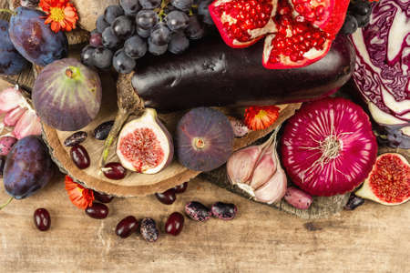 Blue, red and purple food. Culinary background of fruits and vegetables. Fresh figs, plums, onion, eggplant, grape, cabbage, apple, garlic, dogwood, pomegranate, beetroot. Wooden stands and old boardsの写真素材