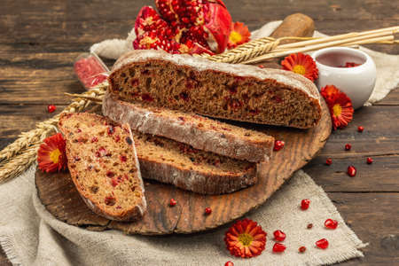 Whole grain bread with cranberry for holidays. Fresh homemade bakery, ripe pomegranate, dry spikelets. Autumn chrysanthemums, vintage wooden background, close upの写真素材