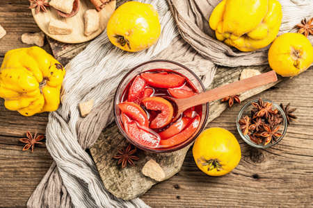 Quince jam or confiture brewed with brown sugar. Ripe whole fruits, sweet dessert, fragrant spices. Trendy wooden stand, old boards background, top viewの写真素材