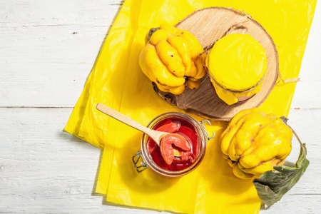 Ripe whole quince and sweet jam from it. Fresh fruit, an essential ingredient for a healthy diet, dessert in a glass jar. Trendy hard light, dark shadow. White wooden background, top viewの写真素材