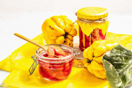 Ripe whole quince and sweet jam from it. Fresh fruit, an essential ingredient for a healthy diet, dessert in a glass jar. Trendy hard light, dark shadow. White wooden background, close upの写真素材