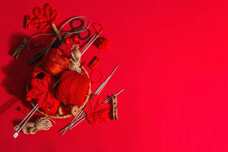 Festive handmade concept. Threads, knitting needles, vintage scissors, autumn decor. Monochrome objects in red colors on a rough background, top viewの写真素材