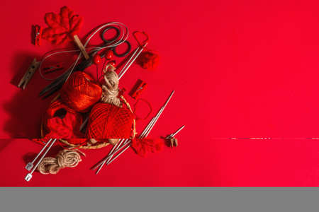 Festive handmade concept. Threads, knitting needles, vintage scissors, autumn decor. Monochrome objects in red colors on a rough background, top viewの写真素材