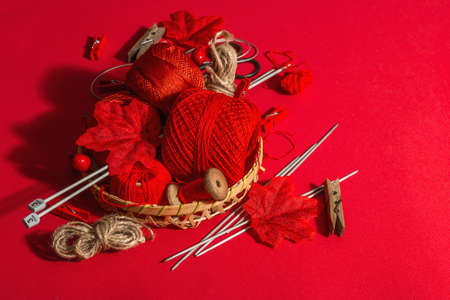 Festive handmade concept. Threads, knitting needles, vintage scissors, autumn decor. Monochrome objects in red colors on a rough background, copy spaceの写真素材