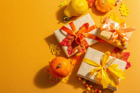 Gift concept in autumn colors. Wrapped boxes, festive fall decor, pumpkin, leaves, and berries. A trendy hard light, dark shadow, orange background, top viewの写真素材