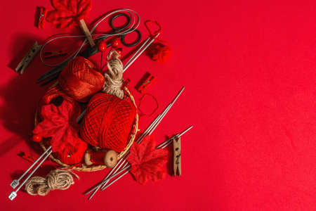 Festive handmade concept. Threads, knitting needles, vintage scissors, autumn decor. Monochrome objects in red colors on a rough background, top viewの写真素材