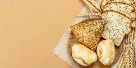 Freshly baked bread with wheat ears, buns, and toasts. Assorted bakery on light beige background....