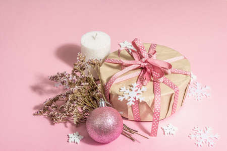 Christmas or New Year gift concept in pink tones. Wrapper box, tied bow, dry flowers, and festive toy. Zero Waste style, trendy hard light, dark shadow, rosy background, copy spaceの写真素材