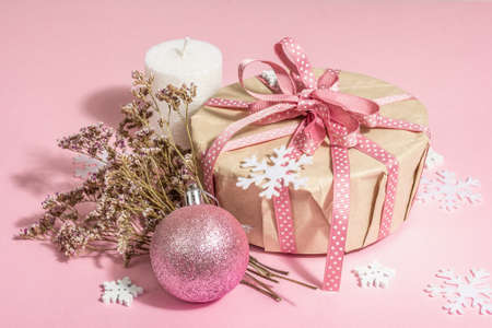 Christmas or New Year gift concept in pink tones. Wrapper box, tied bow, dry flowers, and festive toy. Zero Waste style, trendy hard light, dark shadow, rosy background, close upの写真素材