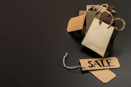 Black Friday Sale concept. Shopping paper bags, handmade tags. Black stone concrete background, trendy hard light, dark shadow, copy spaceの写真素材