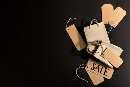 Black Friday Sale concept. Shopping paper bags, handmade tags. Black stone concrete background, trendy hard light, dark shadow, top viewの写真素材