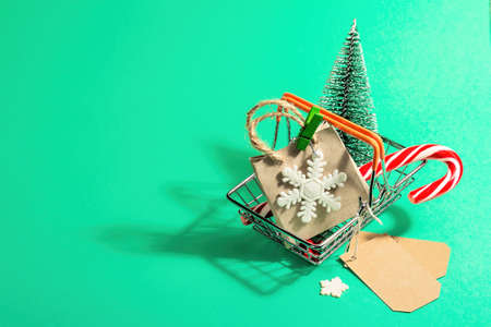 Christmas Sale concept on turquoise background. Shopping basket with fir tree, festive gifts and traditional New Year decor. A trendy hard light, dark shadow. Flat lay, mockup, template, copy spaceの写真素材