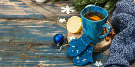 Hot drink with crocheted funny mittens. Traditional winter decor, fir tree branches, snowflakes. Festive seasonal arrangement in blue tones, old wooden background, banner formatの写真素材