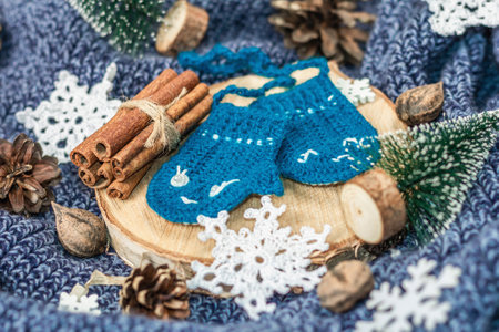 Funny crocheted mittens with traditional New Year decoration. Little firs, crocheted snowflakes, nuts, cinnamon and cones. Wooden stand, cozy knitted sweater arrangement, close upの写真素材