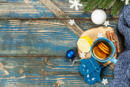 Hot drink with crocheted funny mittens. Traditional winter decor, fir tree branches, snowflakes. Festive seasonal arrangement in blue tones, old wooden background, top viewの写真素材