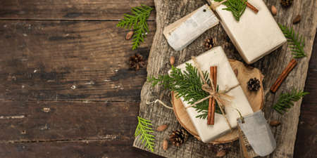 Zero waste gift concept. Christmas or New Year eco-friendly packaging. Festive boxes in craft paper with different organic decorations. Vintage wooden background, banner formatの写真素材