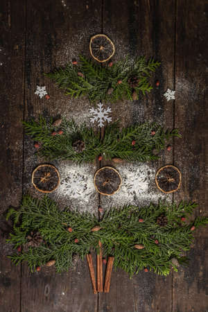 Creative fir tree from evergreen branches, dried lemon slices and snowflakes. Wooden background,...