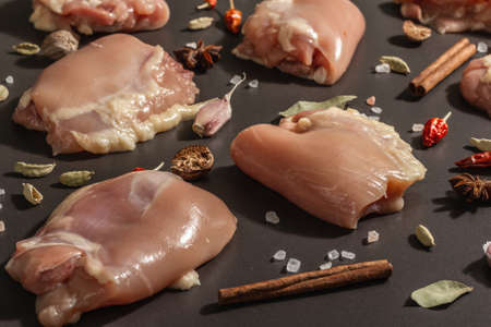 Raw chicken thighs without bones or skin. A useful ingredient for preparing healthy food, spices, garlic. Black stone background, trendy hard light, dark shadow, close upの写真素材
