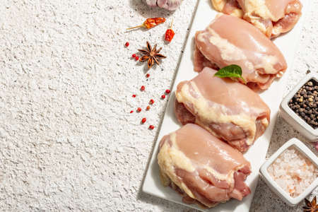 Raw chicken thigh without bones or skin. A useful ingredient for preparing healthy food, spices, garlic. Fashion hard light, dark shadow, light putty background, top viewの写真素材