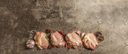 Raw chicken thigh without bones or skin. A useful ingredient for preparing healthy food, spices, garlic. Dark stone background, banner formatの写真素材