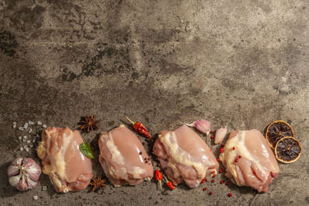 Raw chicken thigh without bones or skin. A useful ingredient for preparing healthy food, spices, garlic. Dark stone background, top viewの写真素材