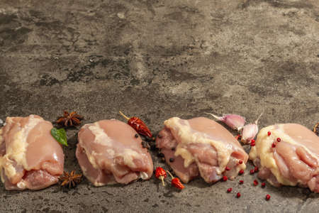 Raw chicken thigh without bones or skin. A useful ingredient for preparing healthy food, spices, garlic. Dark stone background, copy spaceの写真素材