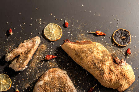 Raw chicken thighs with spices. A useful ingredient for preparing healthy food. Black stone background, trendy hard light, dark shadow, top viewの写真素材