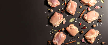 Raw chicken thighs without bones or skin. A useful ingredient for preparing healthy food, spices, garlic. Black stone background, trendy hard light, dark shadow, banner formatの写真素材
