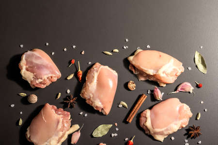 Raw chicken thighs without bones or skin. A useful ingredient for preparing healthy food, spices, garlic. Black stone background, trendy hard light, dark shadow, top viewの写真素材