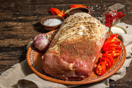 Marinated pork loin. A raw piece of meat for cooking festive food. Hot pepper, spices, rustic style. Trendy hard light, dark shadow. Old wooden background, close upの写真素材