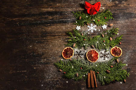 Creative fir tree from evergreen branches, dried lemon slices and snowflakes. Wooden background,...