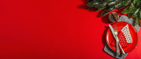 Served Christmas table setting in red tones with vintage cutlery. Evergreen branches, crocheted fir trees, artificial snow. Modern hard light, dark shadow. Flat lay, red background, banner formatの写真素材