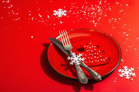 Served Christmas table setting in red tones with vintage cutlery. Crocheted fir tree, artificial snow. Modern hard light, dark shadow. Flat lay, red background, copy spaceの写真素材