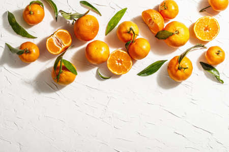 Tangerines (oranges, mandarins, clementines, citrus fruits) with green leaves. Modern hard light, dark shadow. White putty background, creative flat lay, top viewの写真素材