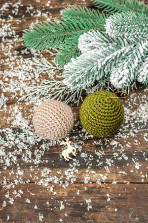 Crocheted Christmas balls and holiday decor. Snow-covered fir tree branches, wooden background. Festive greeting card concept, wallpaper, top viewの写真素材