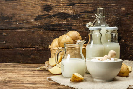 Alternative potato milk, trendy non-dairy drink. Lactose free vegan plant beverage, whole vegetable and dry powder. Wooden background, copy spaceの写真素材