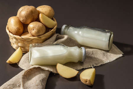 Alternative potato milk, trendy non-dairy drink. Lactose free vegan plant beverage, whole vegetable and dry powder. Modern hard light, dark shadow, black stone background, close upの写真素材