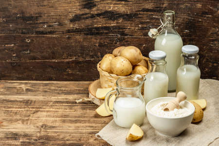 Alternative potato milk, trendy non-dairy drink. Lactose free vegan plant beverage, whole vegetable and dry powder. Wooden background, copy spaceの写真素材