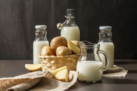 Alternative potato milk, trendy non-dairy drink. Lactose free vegan plant beverage, whole vegetable and dry powder. Modern hard light, dark shadow, black stone background, copy spaceの写真素材