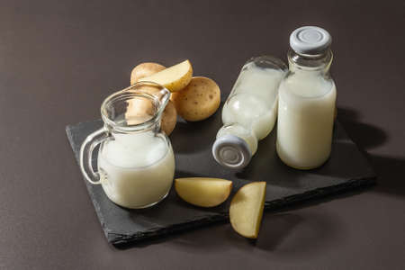 Alternative potato milk, trendy non-dairy drink. Lactose free vegan plant beverage, whole vegetable and dry powder. Modern hard light, dark shadow, black stone background, close upの写真素材